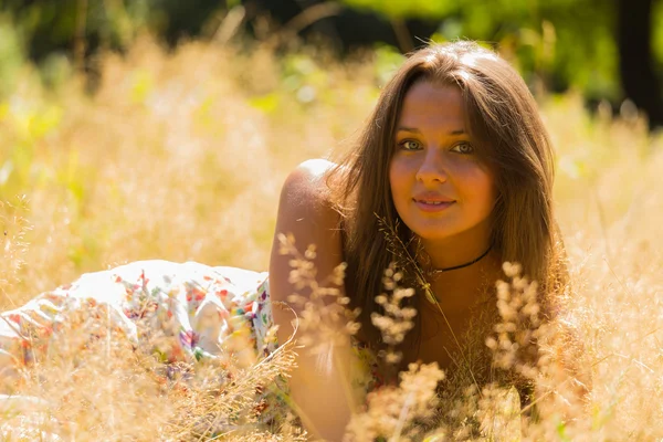 Una chica joven y atractiva en hermoso vestido de verano en medio de prados soleados. Chica alegre tomando el sol en los cálidos rayos del sol de verano. Hermosa imagen de una chica despreocupada . —  Fotos de Stock