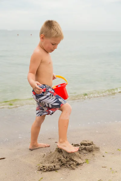 Pantaloncini da ragazzo sulla spiaggia. Bambini che giocano con la sabbia marina. Gioia e divertimento per i bambini. Una bella giornata calda. Foto per riviste e siti web per bambini . — Foto Stock