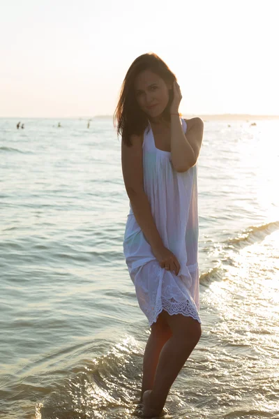 Młoda piękna dziewczyna w białej sukni na plaży. Fotografia piękne dziewczyny na plaży. Dziewczyna pozuje w uwodzicielski sposób. Zdjęcie do podróży i społecznych czasopisma, plakaty i stron internetowych. — Zdjęcie stockowe