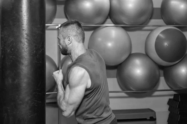 Μυώδης άνδρας στο γυμναστήριο. Ο άνθρωπος χτυπήσει ένα σάκο ζουμπάρισμα, άσκηση. Πυγμαχία προπόνηση, μυών, δύναμη, δύναμη - η έννοια της κατάρτιση δύναμης και πυγμαχία — Φωτογραφία Αρχείου