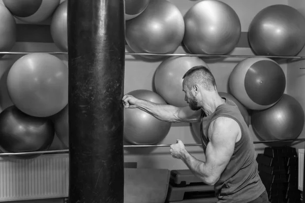 Un uomo muscoloso in palestra. Ha colpito un sacco da boxe, si e 'allenato. Boxe, allenamento, muscoli, forza, potenza: il concetto di allenamento della forza e pugilato — Foto Stock