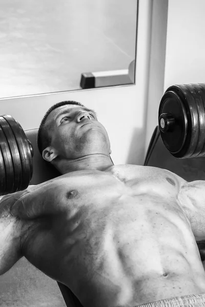 Bank halters in de sportschool. Gespierde man uitvoeren van vermoeiende oefening. Zwart-wit fotografie gespierde man. Foto's voor sportieve tijdschriften en websites. — Stockfoto