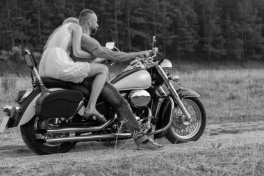 Newlyweds middle of the field on a motorcycle road. Happy couple traveling on a motorcycle. Extraordinary life. Black-and-white photo for social and posters and websites motorcycle magazines. clipart