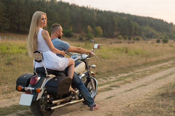 Jovem casal romântico em um campo em uma motocicleta — Fotografia de Stock