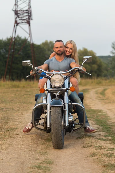 Jovem casal romântico em um campo em uma motocicleta — Fotografia de Stock