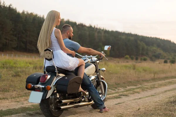Jovem casal romântico em um campo em uma motocicleta — Fotografia de Stock