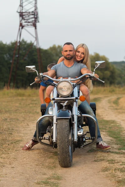 Jovem casal romântico em um campo em uma motocicleta — Fotografia de Stock