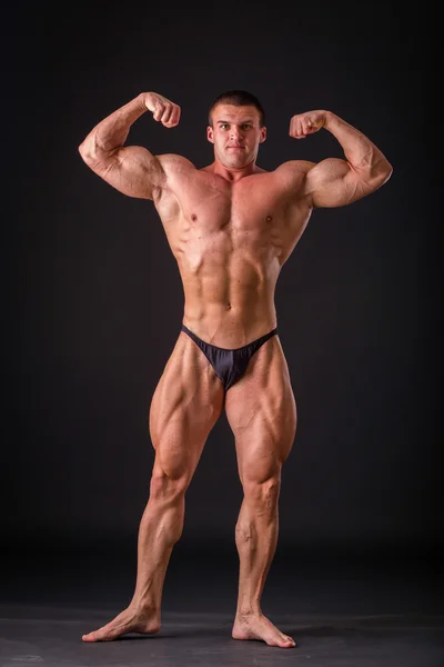 プロのボディービルダーは、暗い背景に彼の体を示しています。筋肉体アスリート。自身のトレーニングとハードの作業によって達成した結果。スポーツの雑誌、ポスター、ウェブサイトのための写真. — ストック写真