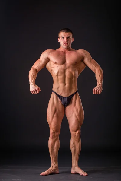 Professional bodybuilder shows his body on a dark background. Muscular body athlete. The result achieved by training and hard work on themselves. Photos for sporting magazines, posters and websites. — Stock Photo, Image