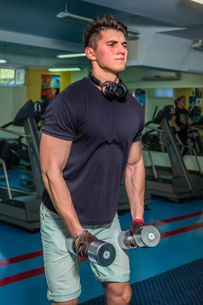 Bodybuilder maakt trainen met halters in de sportschool. Werk op handen vertellen spieren. Vermoeiende work-outs tot een einde. Foto's voor sportieve tijdschriften en websites. — Stockfoto