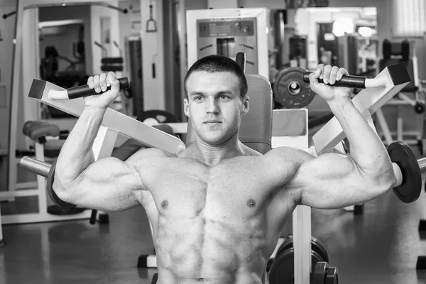 Gespierde man in de sportschool. Werken op de armspieren. Training op een simulator. Vermoeiend werk op zijn lichaam. — Stockfoto