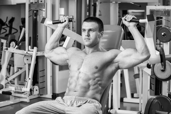 Gespierde man in de sportschool. Werken op de armspieren. Training op een simulator. Vermoeiend werk op zijn lichaam. — Stockfoto