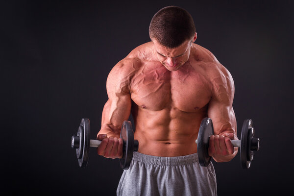 Bodybuilder posing in different poses demonstrating their muscles. Failure on a dark background. Male showing muscles straining. Beautiful muscular body athlete.