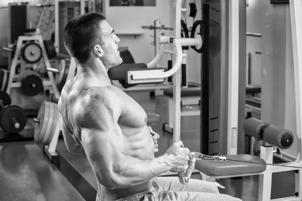 Hombre musculoso en el gimnasio. Trabaja en los músculos del brazo. Entrenamiento en un simulador. Trabajo agotador en su cuerpo . — Foto de Stock