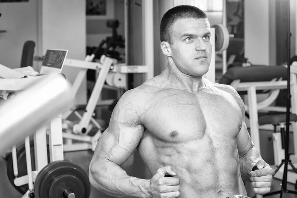 Hombre musculoso en el gimnasio. Trabaja en los músculos del brazo. Entrenamiento en un simulador. Trabajo agotador en su cuerpo . — Foto de Stock