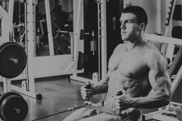 Hombre musculoso en el gimnasio. Trabaja en los músculos del brazo. Entrenamiento en un simulador. Trabajo agotador en su cuerpo . — Foto de Stock