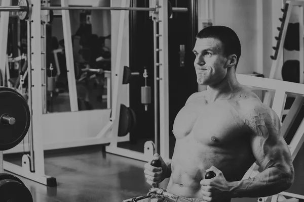 Hombre musculoso en el gimnasio. Trabaja en los músculos del brazo. Entrenamiento en un simulador. Trabajo agotador en su cuerpo . —  Fotos de Stock