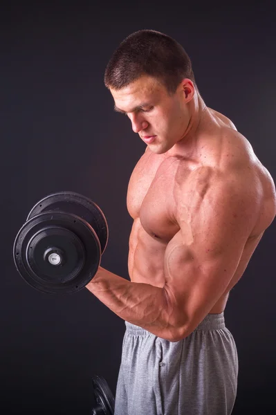 Culturista posa in pose diverse dimostrando i loro muscoli. Fallimento su uno sfondo scuro. Maschio che mostra tensione muscolare. Bellissimo atleta del corpo muscolare . — Foto Stock