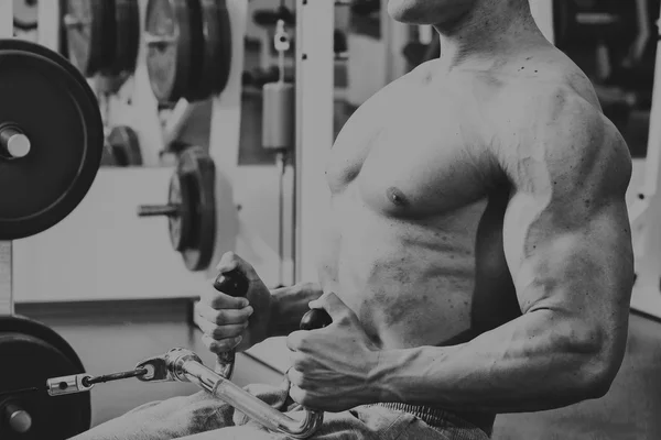 Gespierde man in de sportschool. Werken op de armspieren. Training op een simulator. Vermoeiend werk op zijn lichaam. — Stockfoto