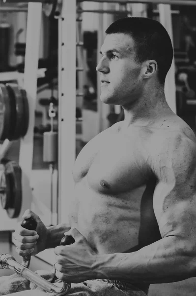 Hombre musculoso en el gimnasio. Trabaja en los músculos del brazo. Entrenamiento en un simulador. Trabajo agotador en su cuerpo . — Foto de Stock