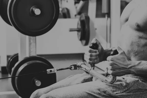 Gespierde man in de sportschool. Werken op de armspieren. Training op een simulator. Vermoeiend werk op zijn lichaam. — Stockfoto