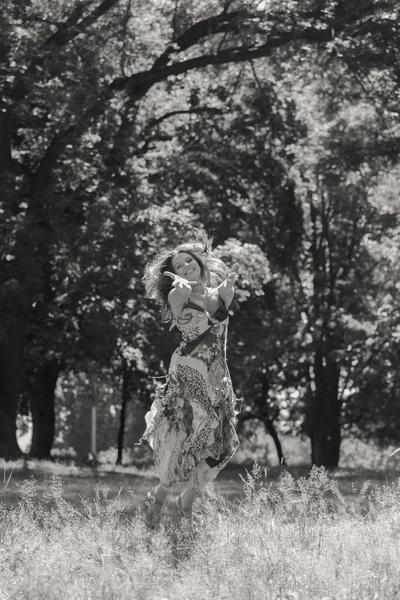 Μελαχρινή νεαρή γυναίκα σε ένα λευκό φόρεμα. Ένα κορίτσι στέκεται στη μέση του πεδίου ροζ λουλούδια σε μια ηλιόλουστη ημέρα. Πεδίο, ανθίζει το ομορφιά, φύση, - η έννοια της χώρας διακοπές. Άρθρο για διακοπές. — Φωτογραφία Αρχείου