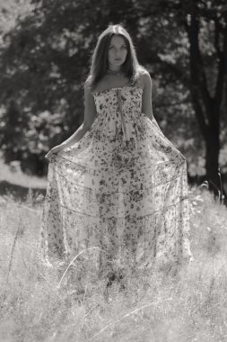 Beyaz elbiseli genç esmer kadın. Bir kız, güneşli bir günde pembe çiçekler tarlanın ortasında duruyor. Alan, çiçekler güzellik, doğa, - ülke tatil kavramı. Tatil hakkında makale.