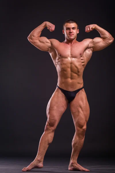 Бодібілдер позує в різних позах, демонструючи свої м'язи. Невдача на темному тлі. Чоловік показує напругу м'язів. Красивий м'язистий спортсмен . — стокове фото