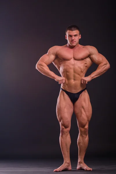 Fisiculturista posando em diferentes poses demonstrando seus músculos. Falha num fundo escuro. Homem mostrando músculos se esforçando. Bonito atleta corpo muscular . — Fotografia de Stock