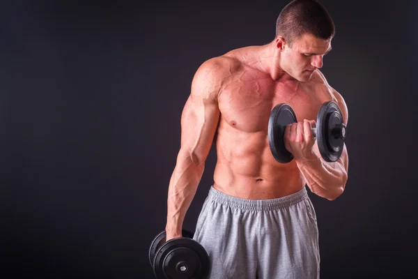 Culturista posa in pose diverse dimostrando i loro muscoli. Fallimento su uno sfondo scuro. Maschio che mostra tensione muscolare. Bellissimo atleta del corpo muscolare . — Foto Stock