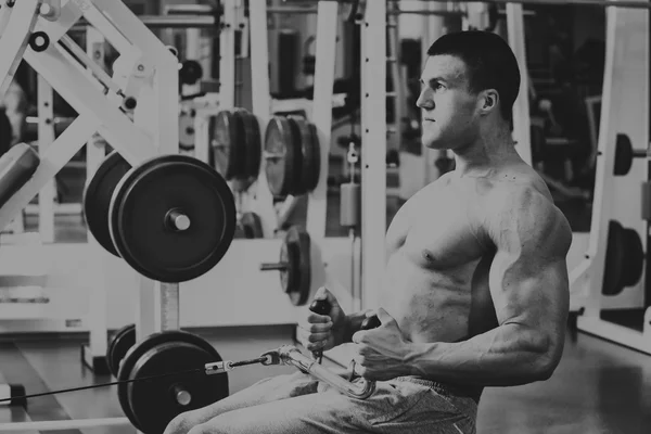 Gespierde man in de sportschool. Werken op de armspieren. Training op een simulator. Vermoeiend werk op zijn lichaam. — Stockfoto