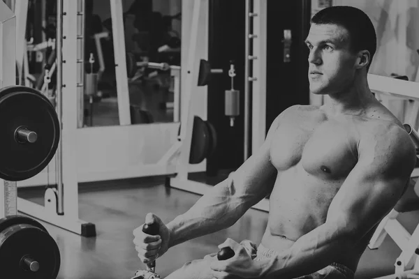 Hombre musculoso en el gimnasio. Trabaja en los músculos del brazo. Entrenamiento en un simulador. Trabajo agotador en su cuerpo . — Foto de Stock