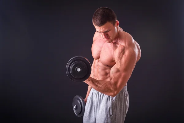 Fisiculturista posando em diferentes poses demonstrando seus músculos. Falha num fundo escuro. Homem mostrando músculos se esforçando. Bonito atleta corpo muscular . — Fotografia de Stock