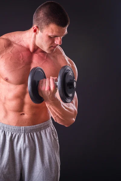 Culturista posa in pose diverse dimostrando i loro muscoli. Fallimento su uno sfondo scuro. Maschio che mostra tensione muscolare. Bellissimo atleta del corpo muscolare . — Foto Stock