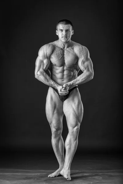 Bodybuilder posing on a black background, black and white photo — Stock Photo, Image