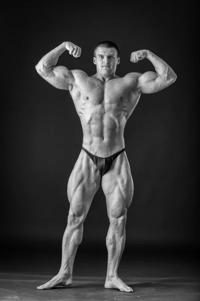 Bodybuilder posing on a black background, black and white photo — Stock Photo, Image