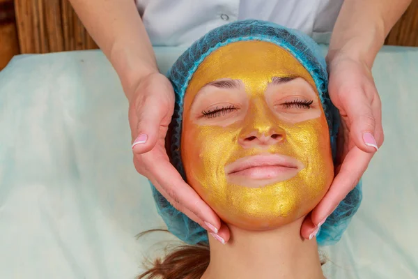 Aplicación de máscaras doradas en la cara del modelo. Procedimientos cosméticos —  Fotos de Stock