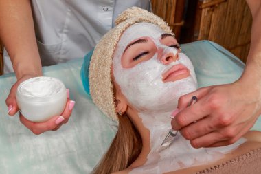 Bir genç kızın yüzüne maske uygulanıyor. Spa salonu yüz cilt