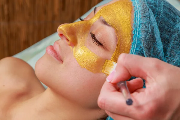 Application of golden masks on the face of the model. Cosmetic procedures — Stock Photo, Image