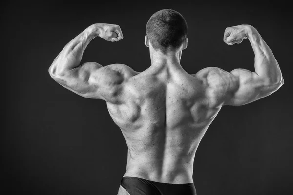 Бодібілдер позує в різних позах, демонструючи свої м'язи. Невдача на темному тлі. Чоловік показує напругу м'язів. Красивий м'язистий спортсмен . — стокове фото