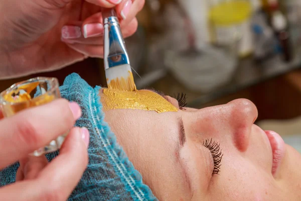 Aplicación de máscaras doradas en la cara del modelo. Procedimientos cosméticos — Foto de Stock