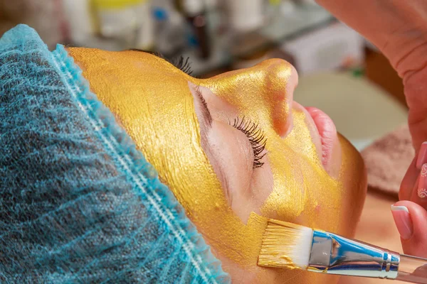 Applicazione di maschere dorate sul volto del modello. Procedure cosmetiche — Foto Stock