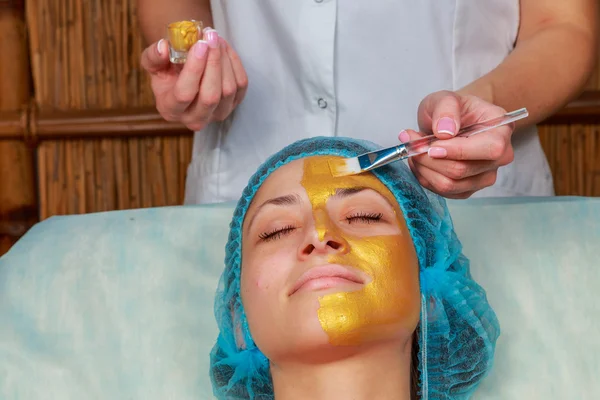 Application of golden masks on the face of the model. Cosmetic procedures — Stock Photo, Image