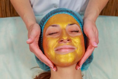 Yüzünde model altın maskesi uygulama. Kozmetik prosedürler