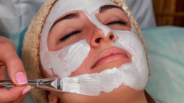 Güzellik salonunda güzellik uzmanı olan bir kız. Güzellik uzmanı kozmetik işlemleri yapıyor. Kozmetik krem uyguluyor. Kozmetoloji, yüz bakımı, güzellik yüz bakımı kavramı. Kozmetoloji hakkında makale.