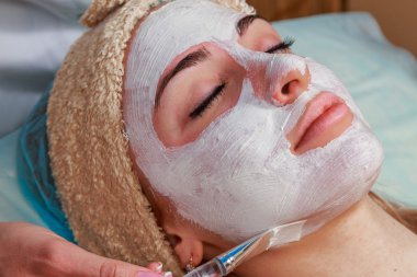 Güzellik salonunda güzellik uzmanı olan bir kız. Güzellik uzmanı kozmetik işlemleri yapıyor. Kozmetik krem uyguluyor. Kozmetoloji, yüz bakımı, güzellik yüz bakımı kavramı. Kozmetoloji hakkında makale.