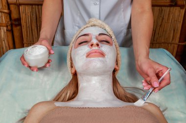 Güzellik salonunda güzellik uzmanı olan bir kız. Güzellik uzmanı kozmetik işlemleri yapıyor. Kozmetik krem uyguluyor. Kozmetoloji, yüz bakımı, güzellik yüz bakımı kavramı. Kozmetoloji hakkında makale.