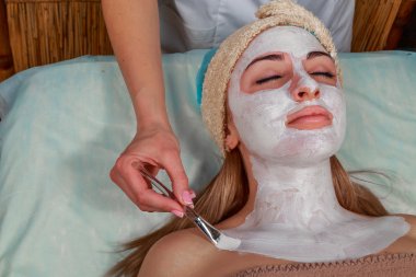 Güzellik salonunda güzellik uzmanı olan bir kız. Güzellik uzmanı kozmetik işlemleri yapıyor. Kozmetik krem uyguluyor. Kozmetoloji, yüz bakımı, güzellik yüz bakımı kavramı. Kozmetoloji hakkında makale.