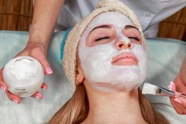 Güzellik salonunda güzellik uzmanı olan bir kız. Güzellik uzmanı kozmetik işlemleri yapıyor. Kozmetik krem uyguluyor. Kozmetoloji, yüz bakımı, güzellik yüz bakımı kavramı. Kozmetoloji hakkında makale.