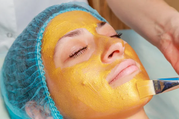 Application of golden masks on the face of the model. Cosmetic procedures — Stock Photo, Image